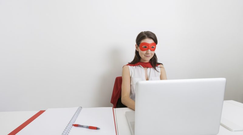 Young businesswoman dressed as superhero using laptop at desk in office